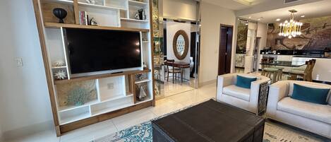 Una sala de estar moderna con un televisor de pantalla plana grande, un sofá, una mesa de centro y un comedor con candelabro.