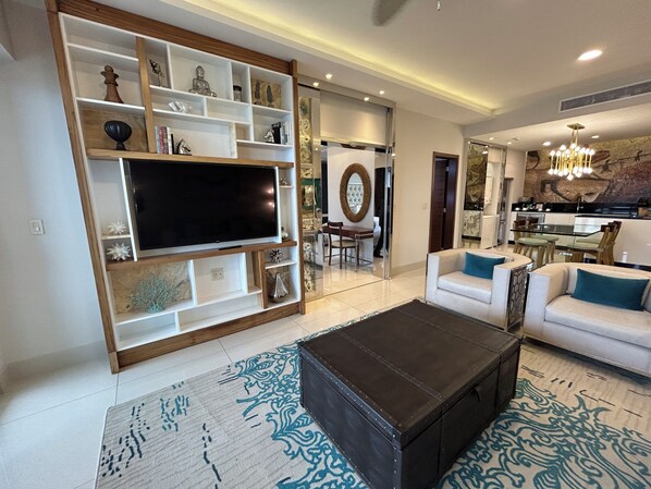 Una sala de estar moderna con un televisor de pantalla plana grande, un sofá, una mesa de centro y un comedor con candelabro.
