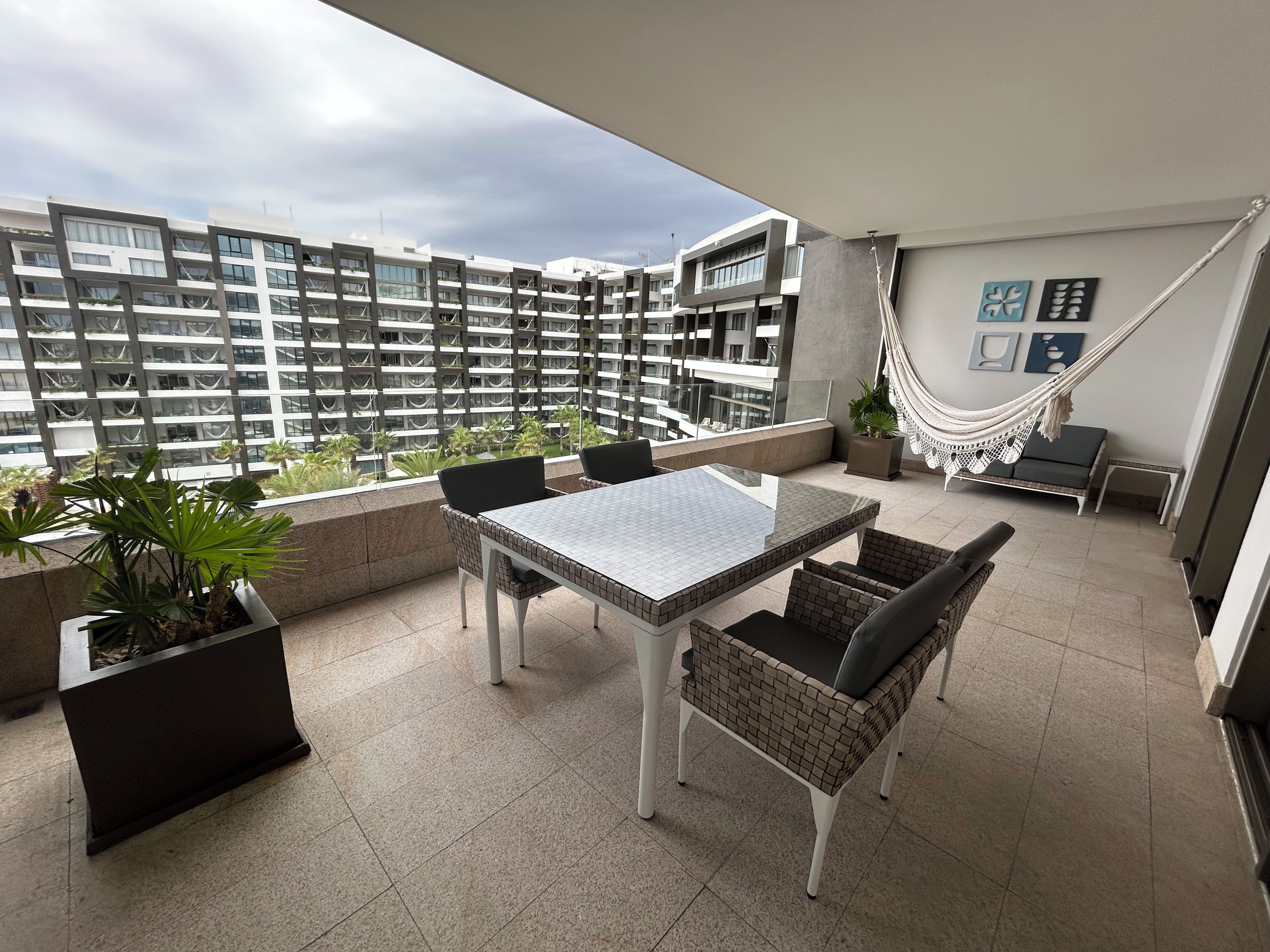 En balkon med et bord, stole, en hængekøje og plantekasser.