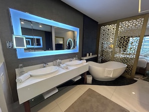Un baño moderno con dos lavamanos, una bañera grande y un separador decorativo.