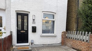 A white brick house with a black front door, a small window, and a mailbox. - 3 Bed House - Sleeps 5 - Garden - Parking - Wifi (Dartford)