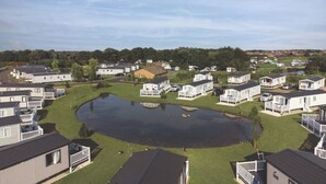 A mobile home park with several single-story homes, a central pond, and a grassy area. - Lakeside Caravan Sleeps 8 - Wifi, Parking, Views (Mablethorpe)