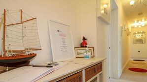 Ein Schreibtisch mit einem Modellschiff, Papieren und einer Whiteboard-Tafel. An der Wand befinden sich Korbwägelchen und ein roter Feuerlöscher.