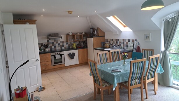A kitchen with wooden cabinets, a dining table with striped chairs, and a skylight above the table. - Shell Hill 3-Bed Apt, Sleeps 6, 15 mins to Beach (Coleraine)
