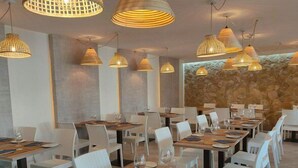 A restaurant with multiple tables, white chairs, and hanging pendant lights.