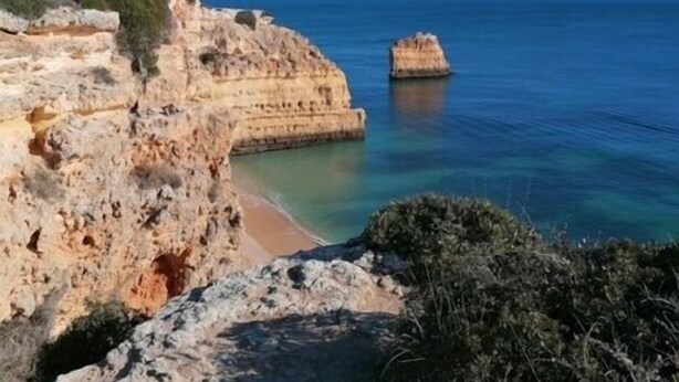 A coastal landscape with rocky cliffs and a clear blue sea.