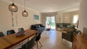 A modern living room with a dining area, featuring a wooden table, chairs, a sofa, and a small round table.