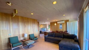 A spacious living area with a wooden wall, a sofa, and two chairs. - A perfect view of Gabo Island. (Mallacoota)
