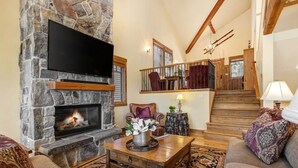 Una chimenea de piedra con un televisor de pantalla plana, una mesa de centro de madera, un sofá y una escalera que conduce a un nivel superior.