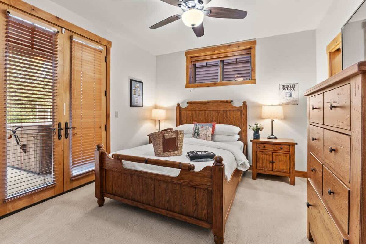 A bedroom with a wooden bed, a ceiling fan, a window with shutters, a nightstand, and a dresser.