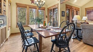 Un comedor con mesa de madera, sillas negras y una araña.