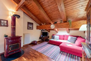 A cozy living room with a wooden ceiling, a red sofa, a patterned rug, and a fireplace. - La Casa di Camus - Central Duplex for 4, Bardonecchia, Italy (Bardonecchia)