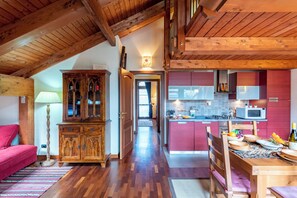 Un interior acogedor con techo de madera, una zona de comedor con una mesa puesta para una comida, una cocina con armarios rojos y una sala de estar con sofá rojo y un mueble.