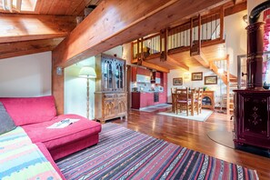Un loft amplio con techo alto, vigas de madera, un sofá rojo, alfombra estampada, un área de comedor y una escalera que sube a un nivel superior.
