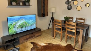 A modern living room with a flat-screen TV, wooden dining table, chairs, a cowhide rug, and a cabinet with plants. - Prime Lodge - Koblenz (Koblenz)