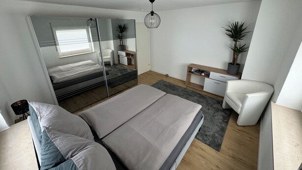 A modern bedroom with a large bed, a desk, a chair, and a mirror. - Prime Lodge - Koblenz (Koblenz)