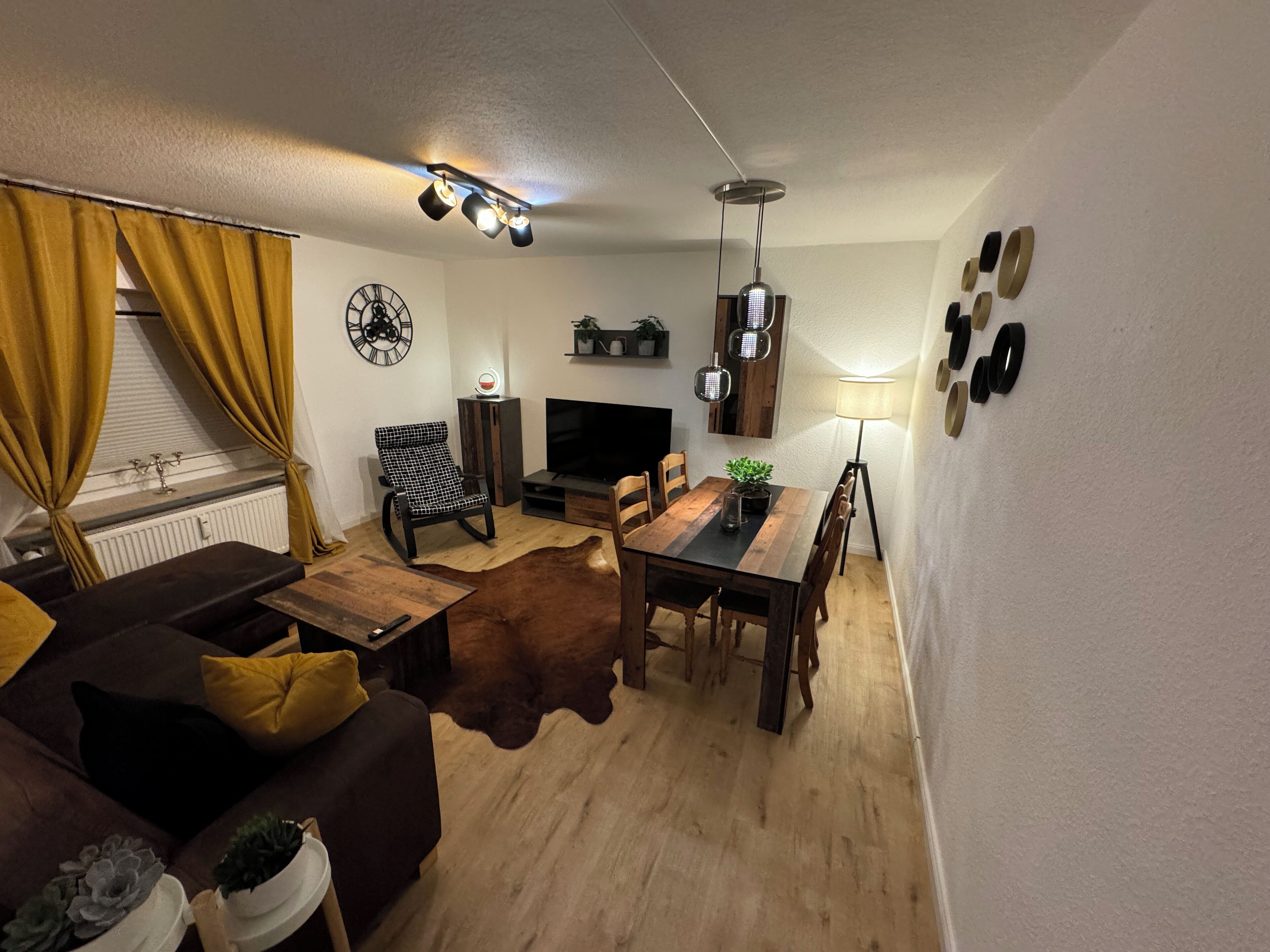 A living room with a sofa, a dining table, a TV, and a leather rug.