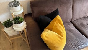 A brown leather sofa with two cushions, a small wooden side table with potted plants, and a white wall in the background. - Prime Lodge - Koblenz (Koblenz)