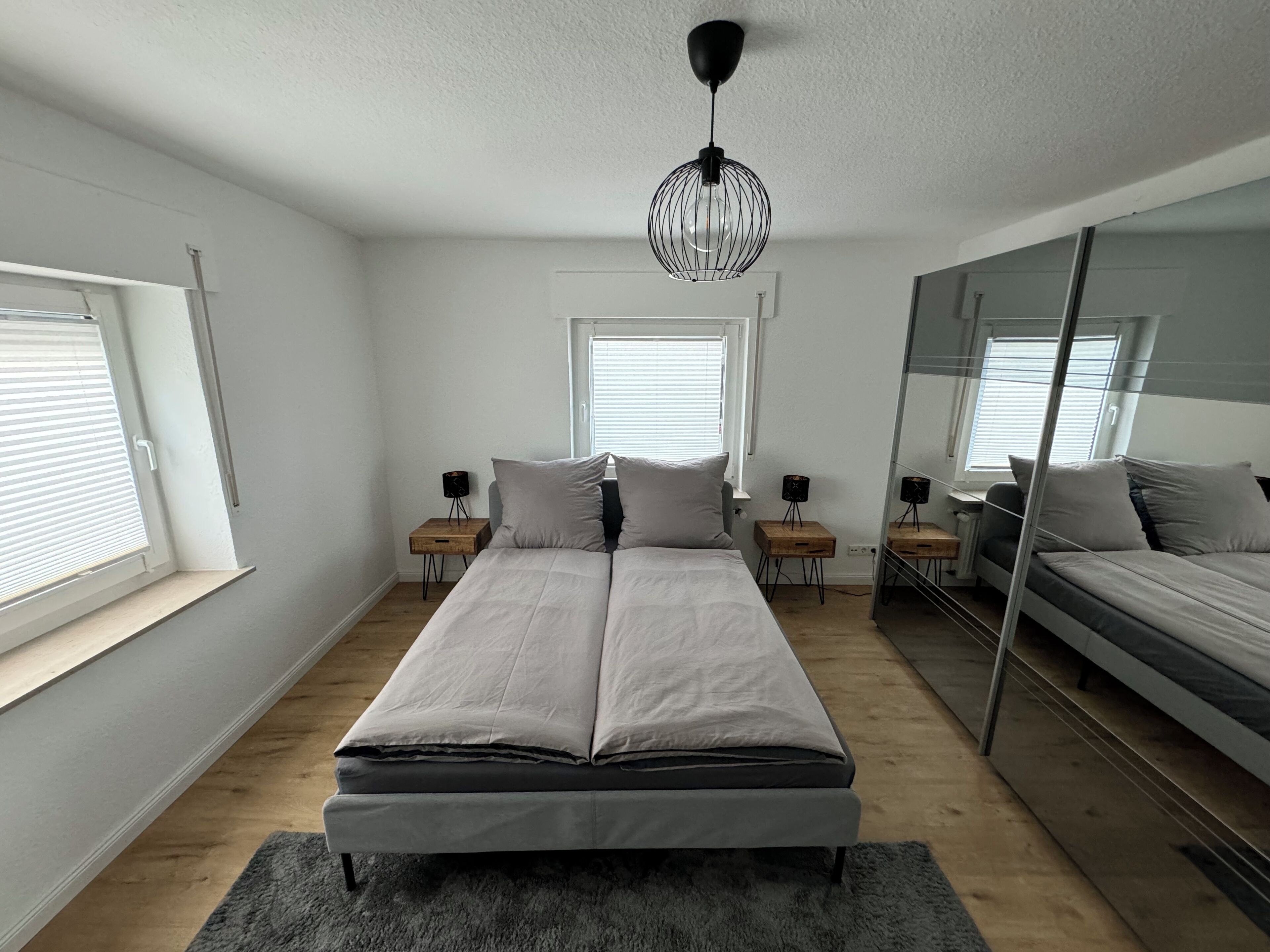 A modern bedroom with a large bed, two bedside tables, a floor lamp, and a mirror.