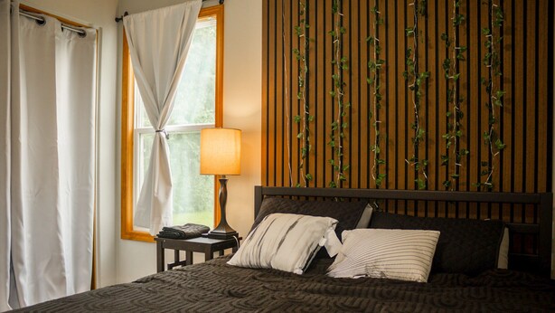 A neatly made bed with a patterned bedspread, a bedside table with a lamp, and a window with curtains.