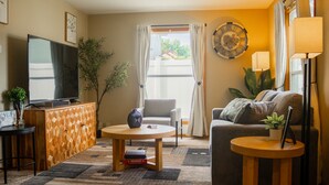 A living room with a sofa, armchair, TV, and a small table with a plant.