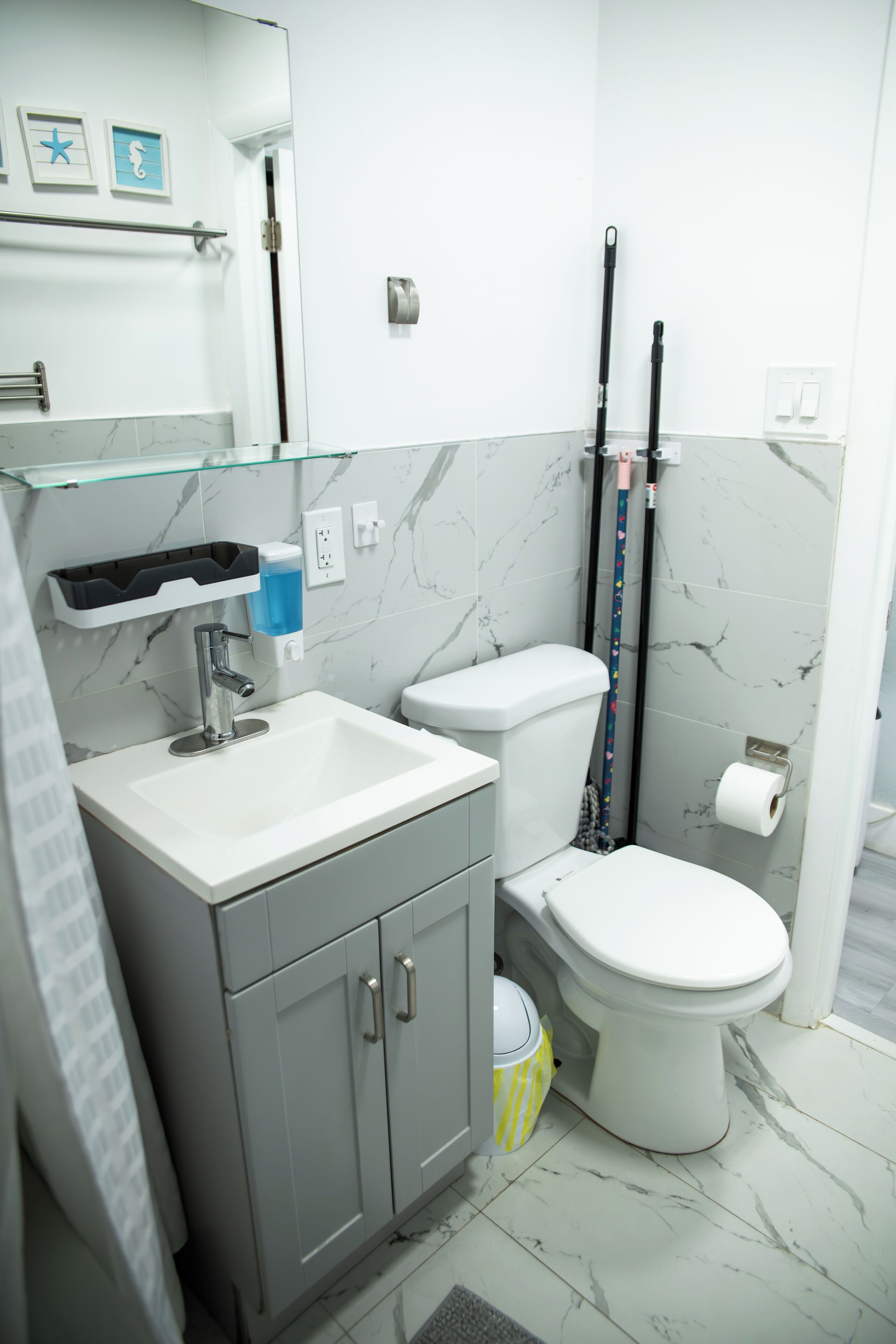 A bathroom with a white sink, a toilet, and a glass shelf above the sink.