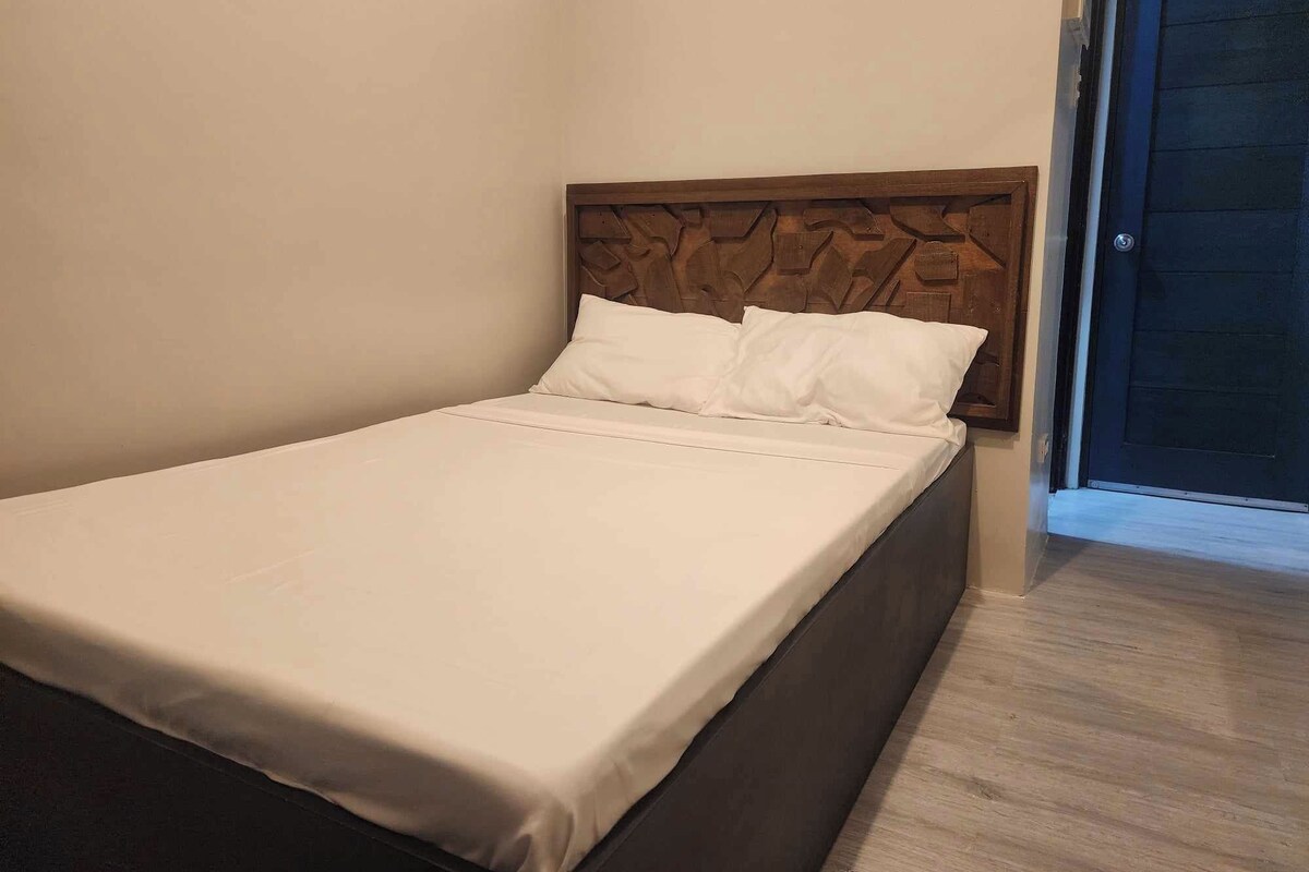 Uma cama de solteiro com cabeceira de madeira em um quarto com paredes lisas e chão de madeira.