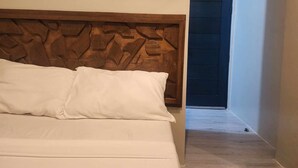 Quarto privativo com cabeceira de madeira e roupa de cama branca.