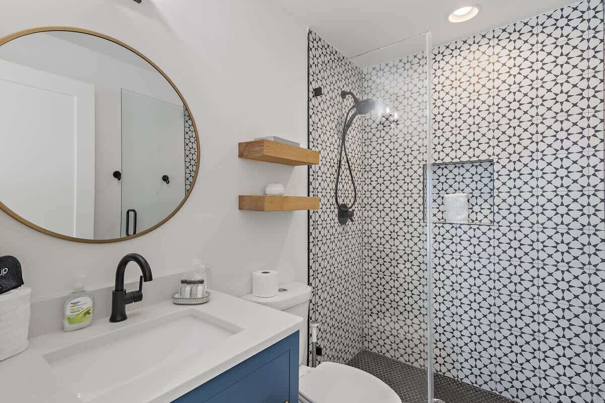 Een badkamer met een ronde spiegel, een wastafel, een douche en behangen wanden.