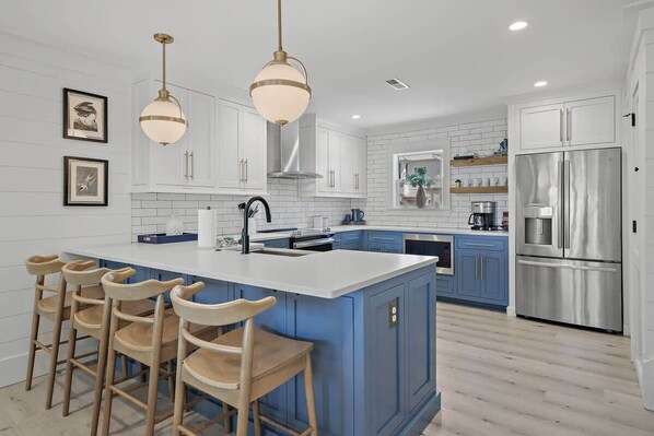 A modern kitchen with a central island, bar stools, stainless steel appliances, and pendant lighting.