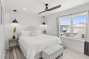 A bedroom with a bed, bedside tables, a ceiling fan, a window with a view, and a plant.