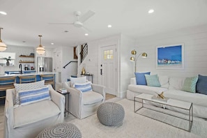 A modern living room with a sofa, armchairs, a coffee table, and a dining area with a kitchen in the background.