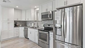 A modern kitchen with white cabinets, stainless steel appliances, and a tiled backsplash. - GULF VIEWS, Community Pool, Honeymoon Retreat, 50 Steps to Beach, Newly Decorated! 'BeeBy The Dunes' (Inlet Beach)