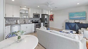 A modern kitchen with white cabinets, a microwave, a refrigerator, and a dining area with a white table and sofa. - GULF VIEWS, Community Pool, Honeymoon Retreat, 50 Steps to Beach, Newly Decorated! 'BeeBy The Dunes' (Inlet Beach)