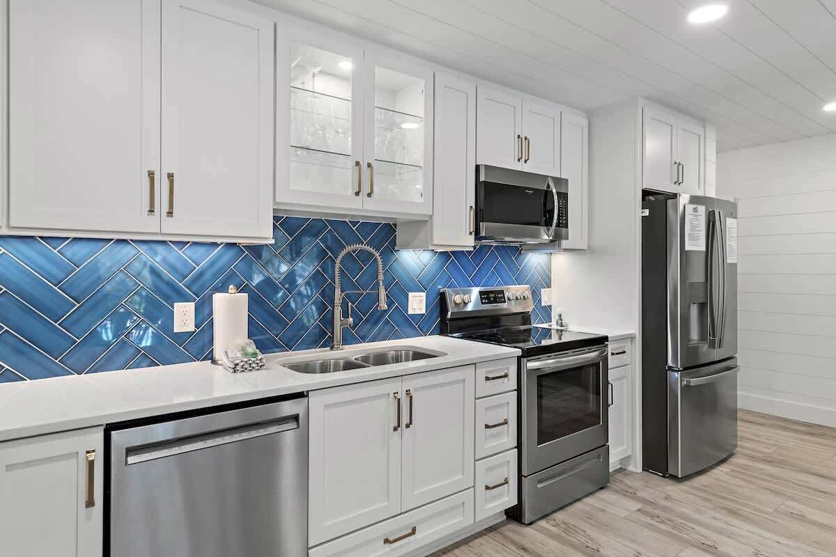Una cocina moderna con armarios blancos, electrodomésticos de acero inoxidable y un salpicadero de azulejos azules.