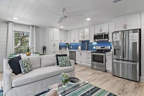A modern kitchen with white cabinets, stainless steel appliances, and a dining area with a white sofa and green cushions.