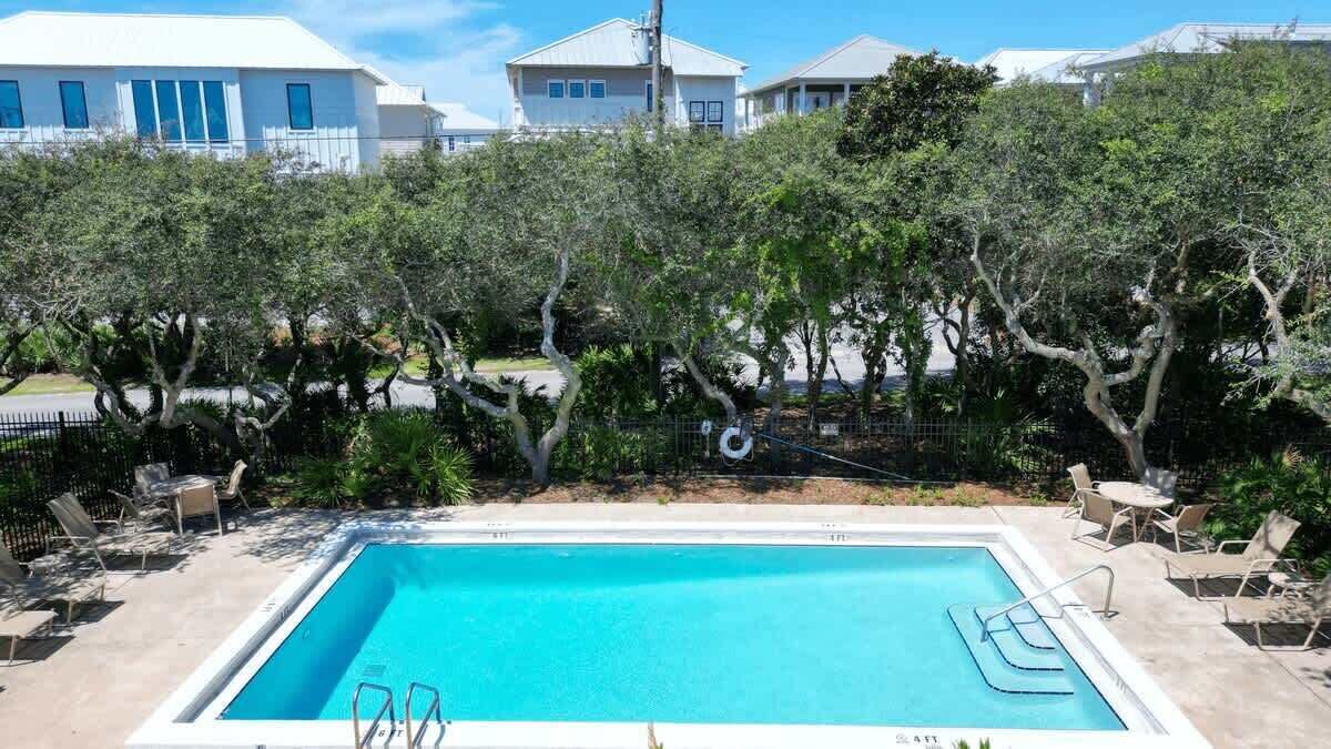 A swimming pool with lounge chairs and a fence, surrounded by trees and buildings.