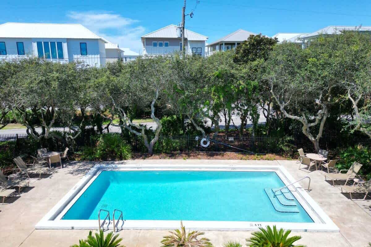 Une piscine rectangulaire bordée de blanc, entourée de chaises longues et de palmiers.