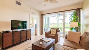 A spacious living room with a flat-screen TV, a wooden cabinet, a sofa, and a coffee table. - Stunning 3BR Naples Condo with Tropical Views (Naples)