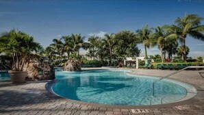 A swimming pool with a curved edge, surrounded by palm trees and a rocky outcrop. - Stunning 3BR Naples Condo with Tropical Views (Naples)
