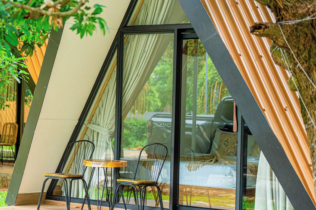 A modern, triangular-shaped building with a glass door and windows, two wooden tables, and four chairs outside.