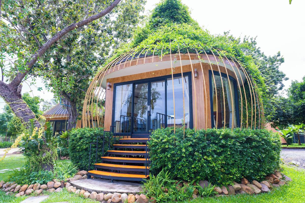 A modern, dome-shaped building surrounded by lush greenery, with a staircase leading to the entrance.