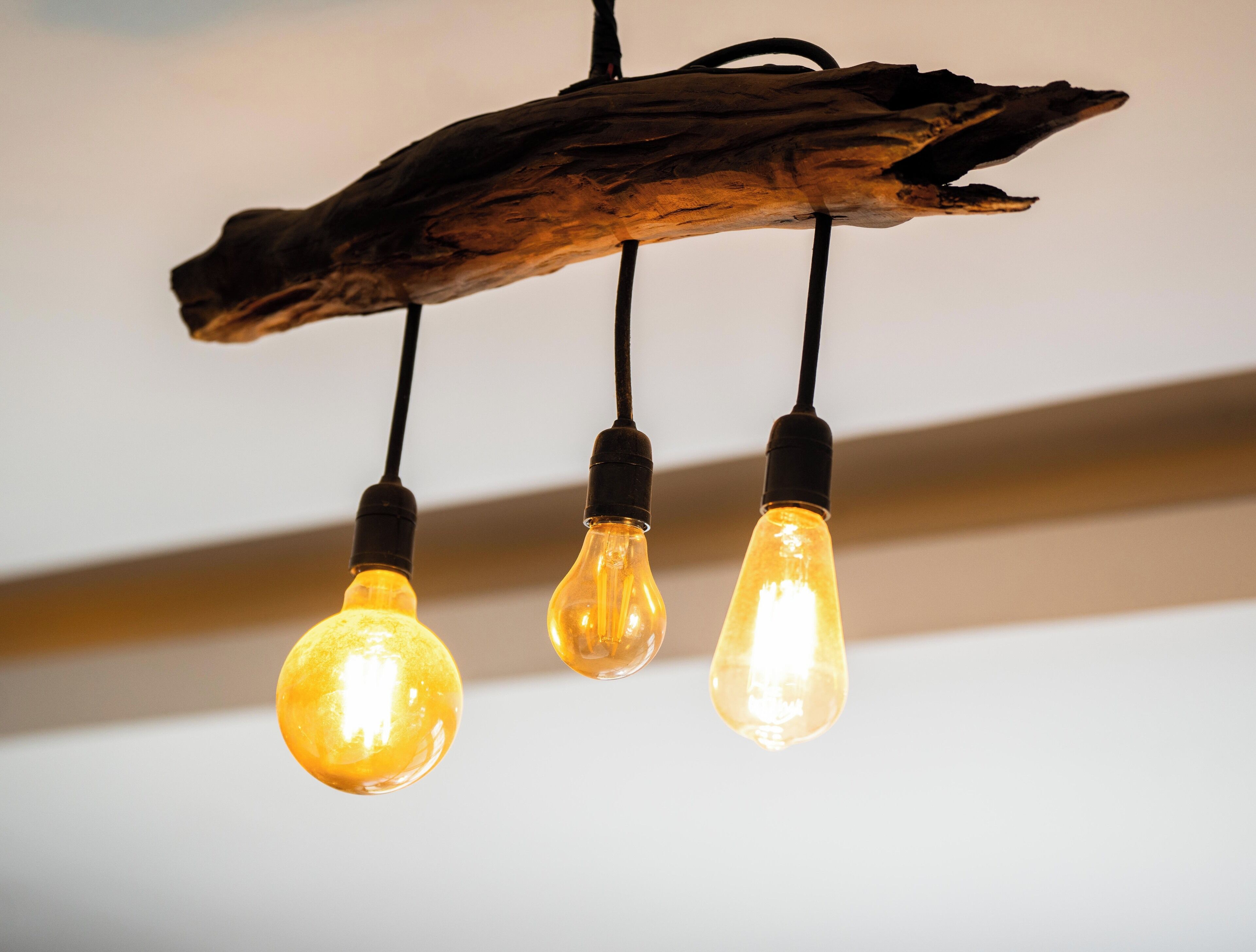 Three light bulbs hanging from a wooden branch.
