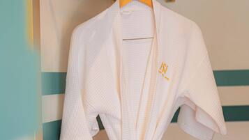 A white robe with a tied knot at the waist, hanging on a wooden hanger against a wall with a striped pattern.