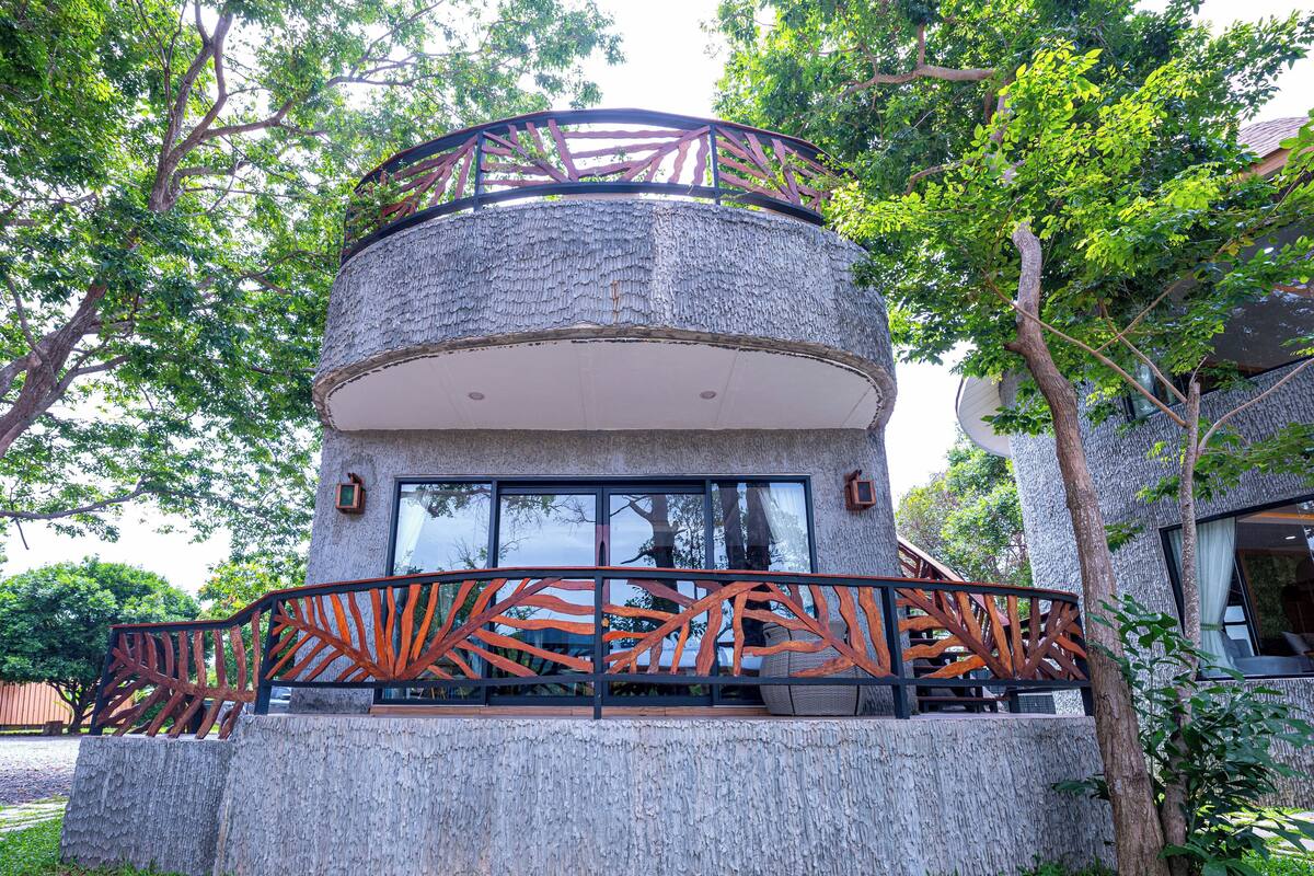 A circular stone structure with a metal railing, surrounded by grass and trees.