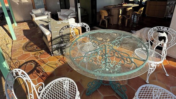 Een open woonkamer met een eettafel met glazen blad, omringd door witte metalen stoelen, een bank en een keuken met houten kasten en een fornuis.