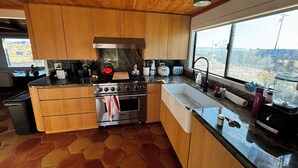A modern kitchen with wooden cabinets, a stainless steel stove, and a large window offering a view of the landscape. - Designer  2-bedroom house in wonderful Landers with AC, WiFi 365 views 2.5 acres (Landers)