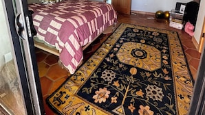 A bedroom with a bed, a wooden ceiling, a patterned rug, and a door leading to another room. - Designer  2-bedroom house in wonderful Landers with AC, WiFi 365 views 2.5 acres (Landers)