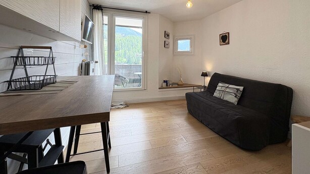 A cozy room with a wooden table, a black sofa, a small window, and a ceiling light fixture. - 2-person studio with superb view of the slopes (LES ORRES 1650)