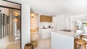 A modern kitchen with white cabinetry, a central island with stools, a wine rack, and a staircase leading to another level.